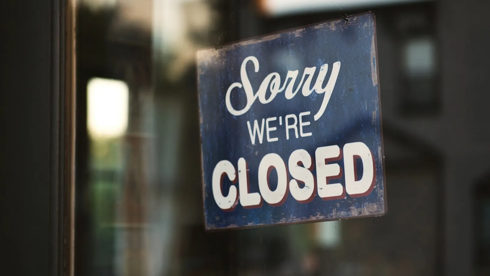 A "Sorry, we're closed" sign hanging on a glass shop door, representing closing a company in the UAE