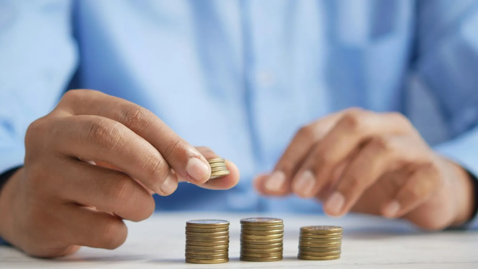 A hand stacking gold and silver coins on a table, representing an owner taking profit out of a UAE company