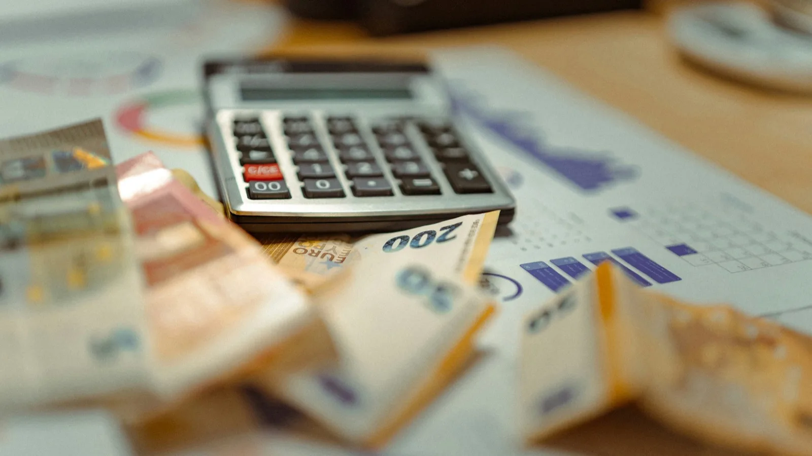 Une calculatrice, des billets et des graphiques financiers imprimés sur un bureau, évoquant la préparation du calcul de l'impôt