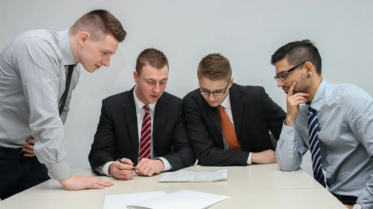Four men in an office reviewing papers on a table, as in a meeting with the auditor Four men in an office reviewing papers on a table, as in a meeting with the auditor