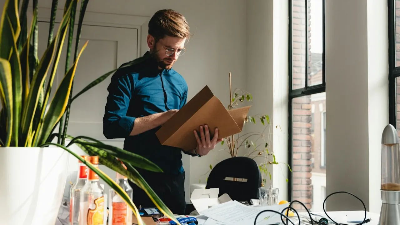 A man in an office holding a cardboard box while clearing out the workspace