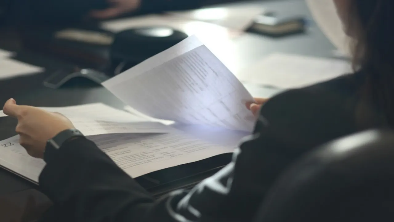 A person at a table reading through a printed document, the way a compliance officer checks a company file