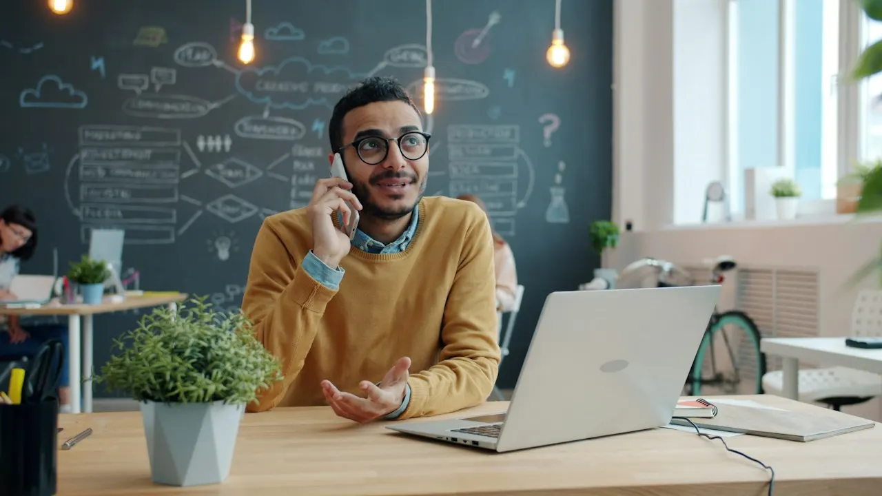 A man on the phone at his desk with a laptop open, following up with the bank