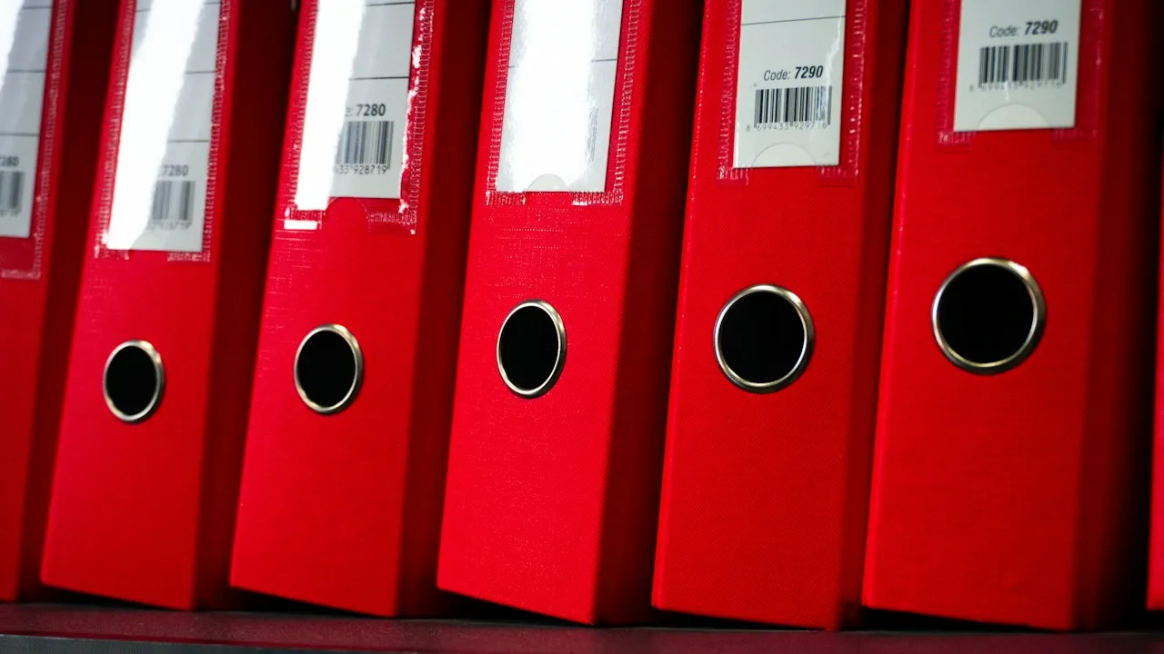 Une rangée de classeurs rouges étiquetés sur une étagère de bureau Une rangée de classeurs rouges étiquetés sur une étagère de bureau