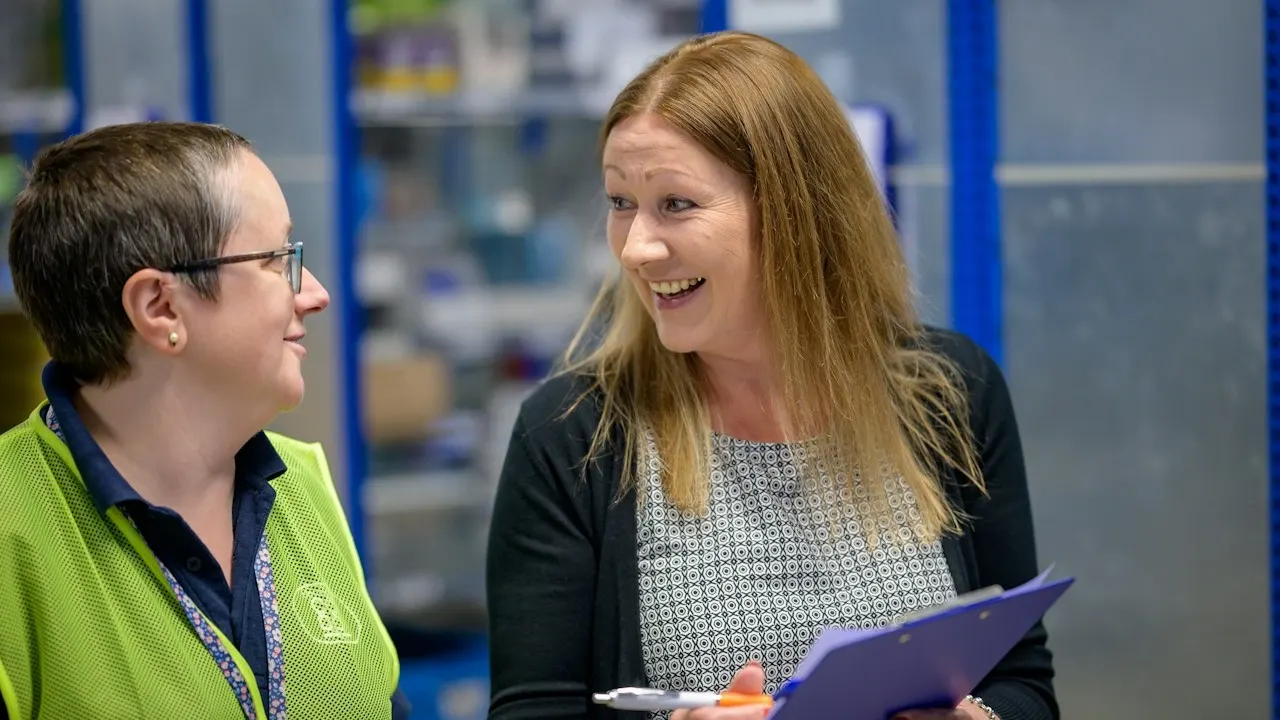 Two colleagues with a clipboard talking in a warehouse during a supplier visit